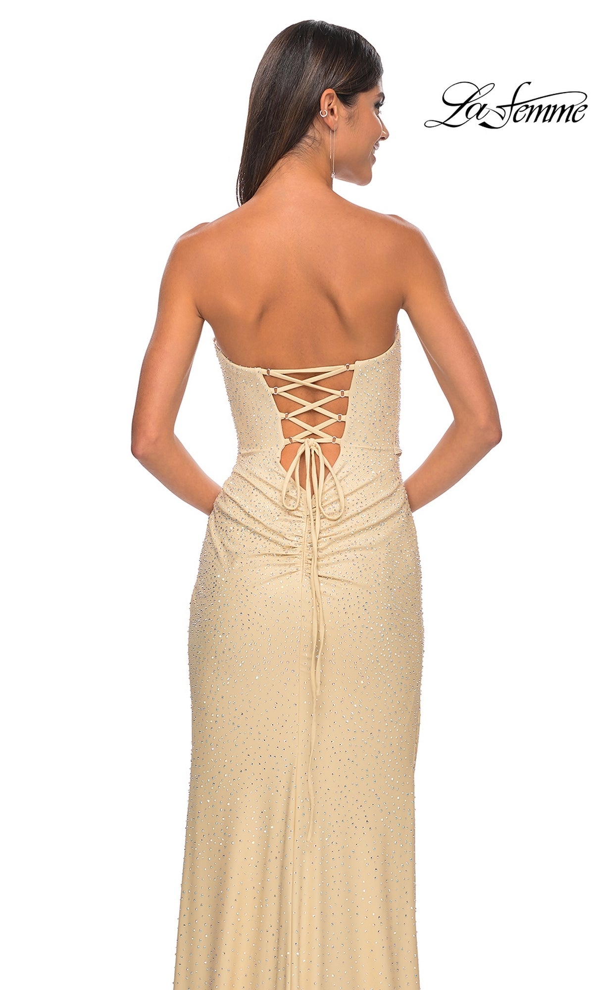 A woman is shown from behind wearing the La Femme Twist Strapless Long Prom Dress 32175 in light beige, featuring a beaded bodice, lace-up back, and subtle sparkly details. The